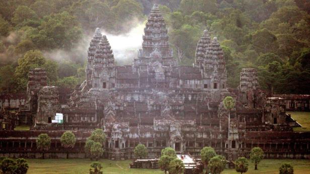 Angkor Wat, eine Tempelanlage in Kambodscha, umgeben von Bäumen und leichtem Nebel.