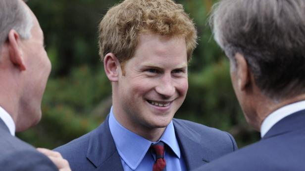 Prinz Harry lächelt im Gespräch mit zwei Männern.