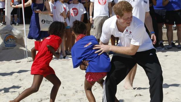 Prinz Harry spielt mit zwei Kindern am Strand.