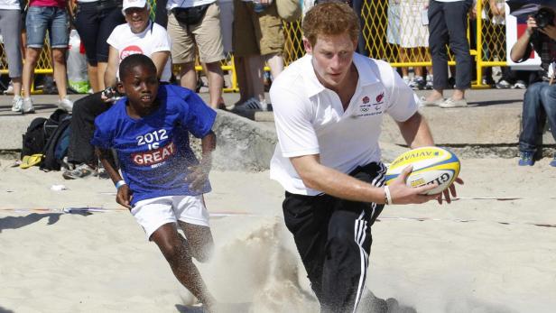 Prinz Harry spielt mit einem Jungen Rugby am Strand.