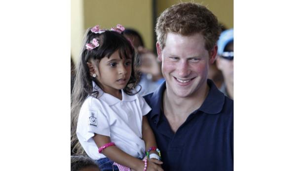 Prinz Harry hält ein kleines Mädchen mit Schmetterlingsspangen im Arm.