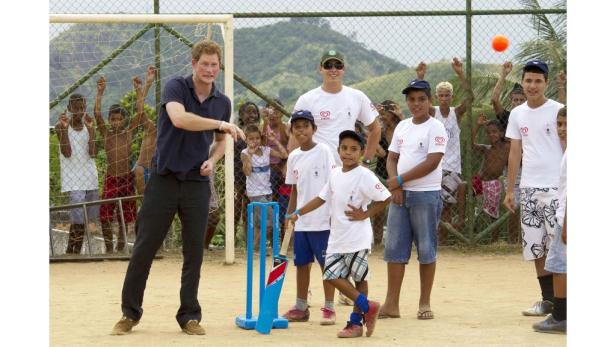 Prinz Harry spielt mit einer Gruppe von Kindern Cricket.
