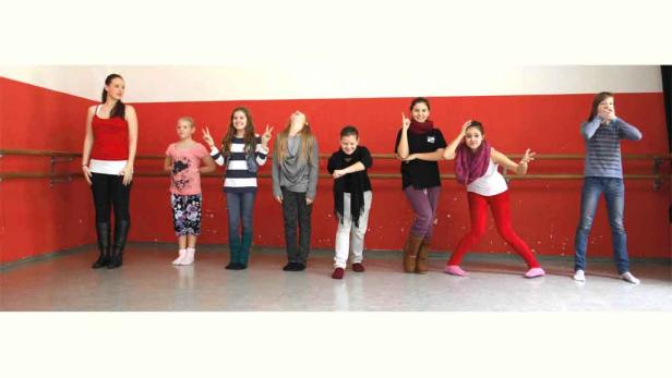 Eine Gruppe junger Frauen posiert in einem Tanzstudio vor einer roten Wand.