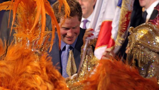 Prinz Harry inmitten von Karnevalskostümen und einer Flagge.