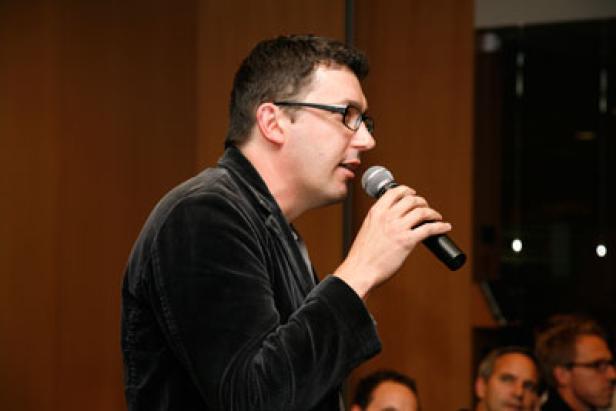 Ein Mann mit Brille spricht in ein Mikrofon vor Publikum.