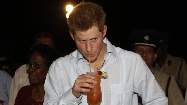 Prinz Harry trinkt mit einem Strohhalm einen Cocktail.