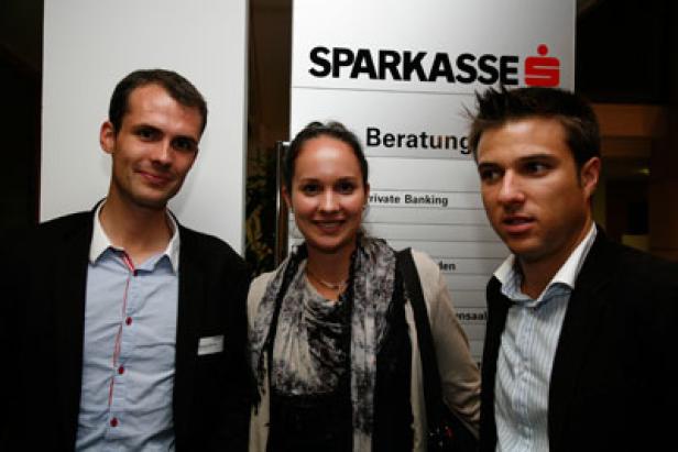 Drei Personen posieren vor einem Schild der Sparkasse.