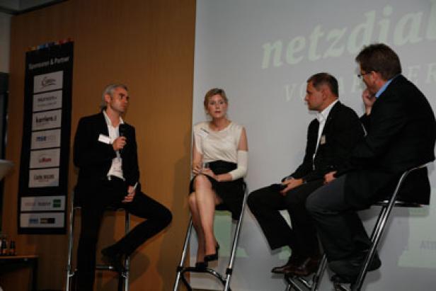 Vier Personen sitzen auf einer Bühne während einer Podiumsdiskussion.