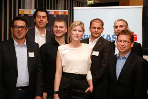 Eine Gruppe von sieben Personen posiert für ein Gruppenfoto vor einem Sparkassen-Banner.