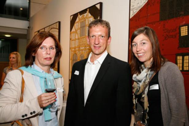 Drei Personen posieren vor Kunstwerken auf einer Vernissage.