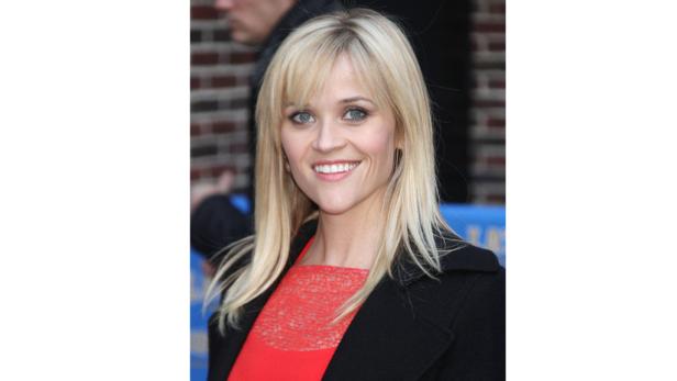Reese Witherspoon lächelt in einem roten Kleid und einem schwarzen Mantel.
