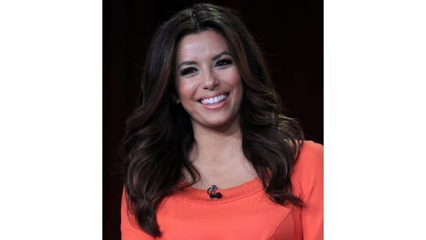 Eva Longoria lächelt in einem orangefarbenen Kleid.