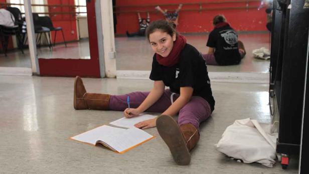 Ein Mädchen sitzt auf dem Boden eines Tanzstudios und schreibt in ein Heft.