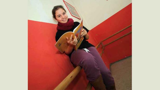 Ein junges Mädchen sitzt auf einem Treppengeländer und liest ein Buch.