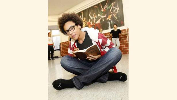 Ein junger Mann mit Brille sitzt auf dem Boden und liest ein Buch.