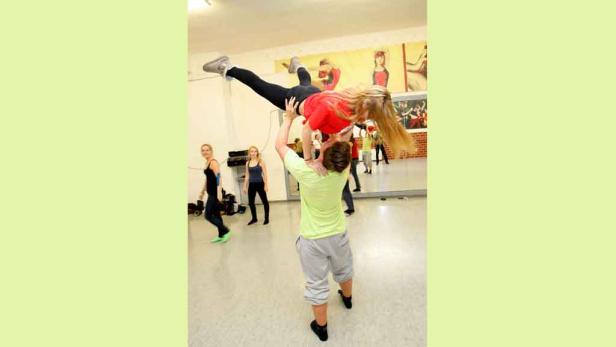 In einem Tanzstudio hebt ein Mann eine Frau hoch in die Luft.