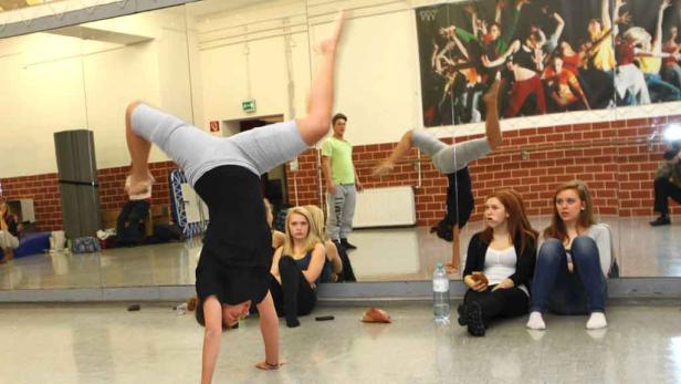 In einem Tanzstudio macht ein Mädchen einen Handstand, während andere zusehen.