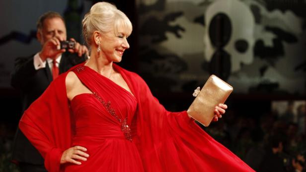 Helen Mirren in einem roten Kleid posiert mit einer goldenen Handtasche auf dem roten Teppich.