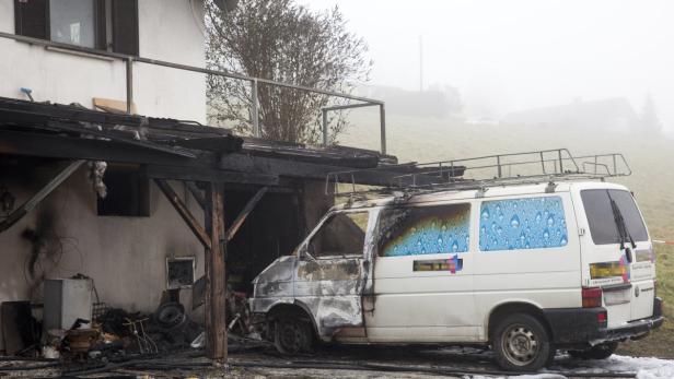 Ein ausgebrannter Lieferwagen steht vor einem beschädigten Haus.