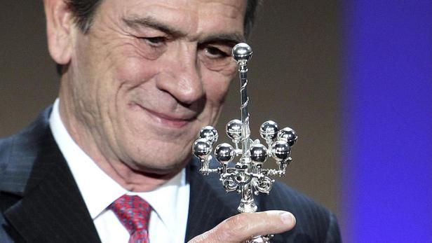 Tommy Lee Jones hält eine silberne Trophäe mit kugelförmigen Verzierungen.