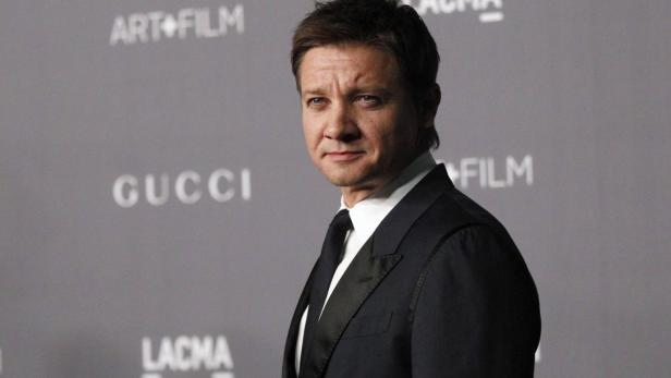Jeremy Renner posiert auf einer Veranstaltung vor einer Wand mit Logos.
