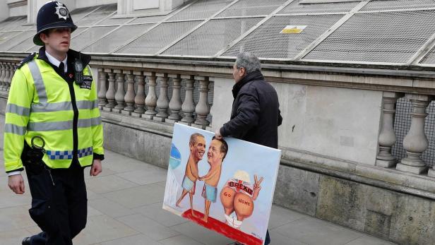 Ein Polizist geht an einem Mann vorbei, der ein Gemälde mit Obama, Cameron und einer Brexit-Karikatur trägt.