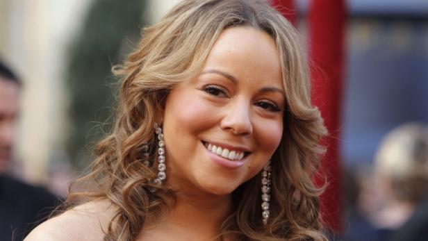Ein Porträt der lächelnden Sängerin Mariah Carey mit langen, gewellten Haaren und auffälligen Ohrringen.