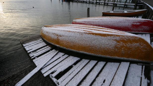 Zwei Kanus liegen schneebedeckt auf einem Holzsteg am Ufer eines Sees.