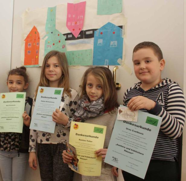 Vier Kinder präsentieren stolz ihre Dankesurkunden vor einem Wandbild mit bunten Häusern.