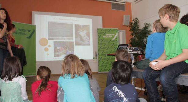 Eine Gruppe Kinder sitzt vor einer Leinwand und schaut einer Präsentation zu.