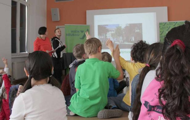 Eine Gruppe von Kindern sitzt vor einer Leinwand und hebt die Hände.