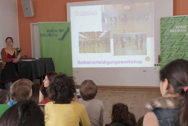 Eine Frau hält einen Vortrag über Selbstverteidigung vor einer Gruppe von Kindern.