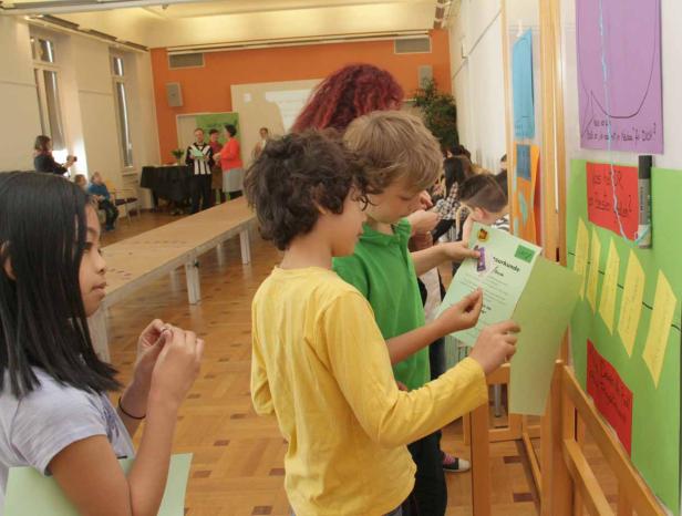 Kinder betrachten eine Ausstellung mit bunten Plakaten und Auszeichnungen.