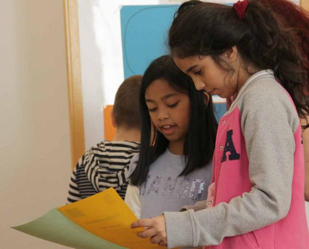 Zwei Mädchen betrachten gemeinsam ein gelbes Blatt Papier.