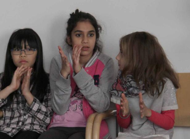 Drei Mädchen sitzen nebeneinander und klatschen in die Hände.