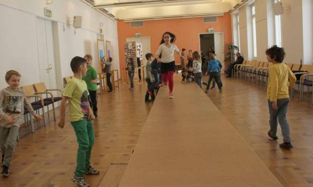 Eine Gruppe Kinder spielt in einem Raum mit einem improvisierten Laufsteg.