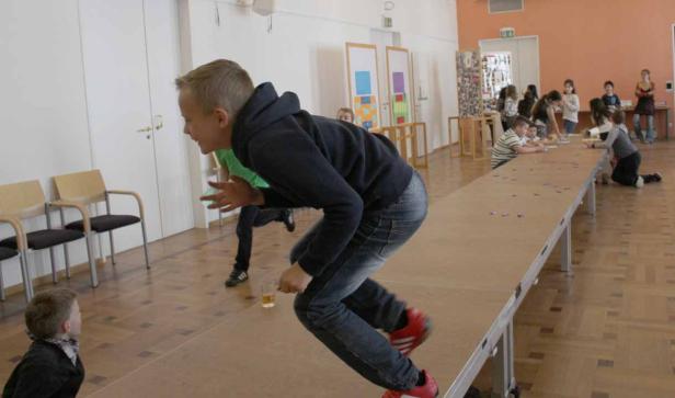 Ein Junge balanciert auf einem langen Tisch in einem Raum voller Kinder.