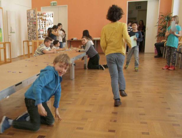 Eine Gruppe Kinder spielt in einem hellen Raum mit Parkettboden.