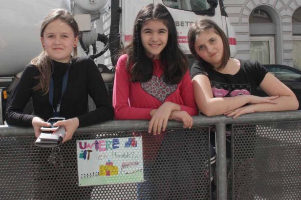 Drei junge Mädchen stehen an einer Absperrung vor einem LKW.