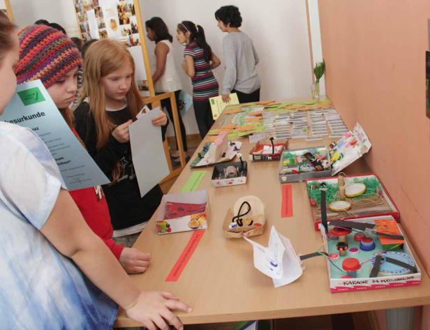 Kinder betrachten auf einem Tisch ausgestellte Kunstprojekte aus recycelten Materialien.