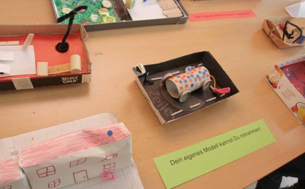 Auf einem Tisch stehen mehrere selbstgebastelte Modelle aus Kartons und anderen Materialien.