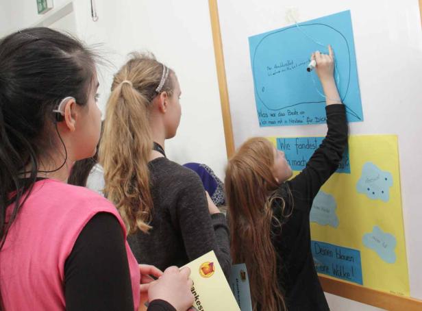 Kinder schreiben und lesen auf Plakaten mit Fragen und Antworten.