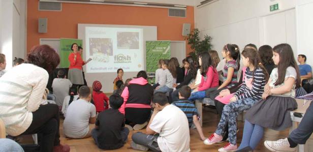 Eine Frau hält eine Präsentation vor einer Gruppe von Kindern in einem Raum.