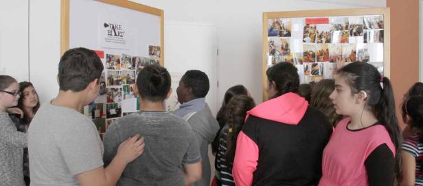 Eine Gruppe von Schülern betrachtet Fotos auf zwei Pinnwänden.