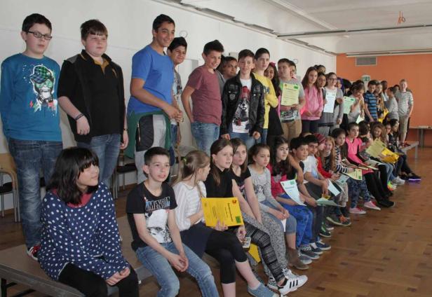 Eine Gruppe von Schülern sitzt und steht mit ihren Zertifikaten in einem Raum.