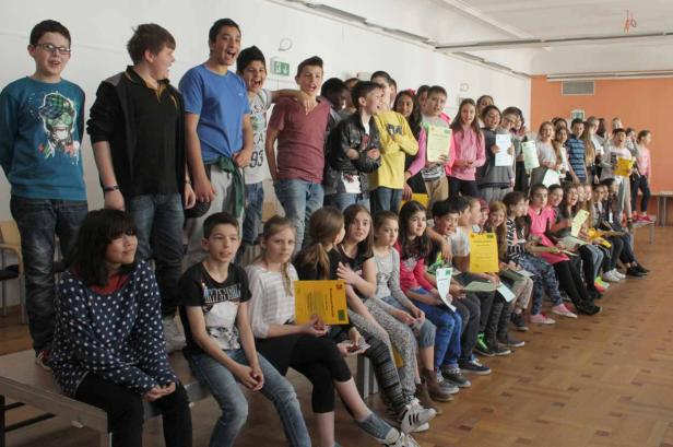 Eine Gruppe von Schulkindern sitzt und steht mit ihren Urkunden in einem Raum.