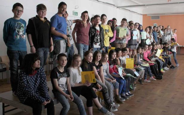 Eine Gruppe von Schülern sitzt und steht mit ihren Zertifikaten in einem Raum.