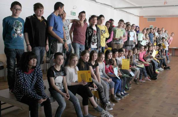 Eine Gruppe von Schulkindern sitzt und steht mit ihren Urkunden in einem Raum.