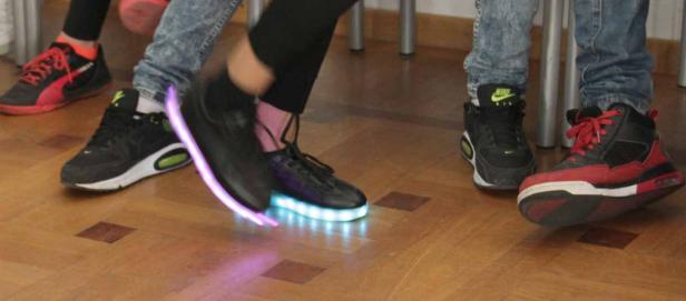 Mehrere Personen tragen verschiedene Turnschuhe, darunter ein Paar mit LED-Leuchten an der Sohle.