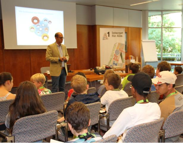 Ein Mann hält eine Präsentation vor einer Gruppe von Kindern und Jugendlichen.